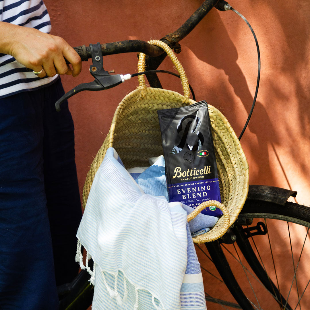 Bicycle basket with a bag of Botticelli coffee and a towel against a red wall.