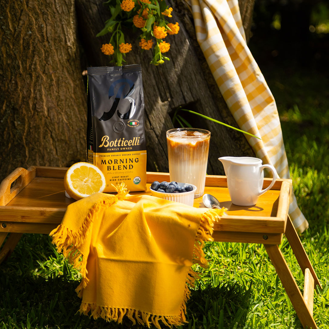 Botticelli coffee bag with a cup of coffee, lemon, and blueberries on a wooden tray outdoors.
