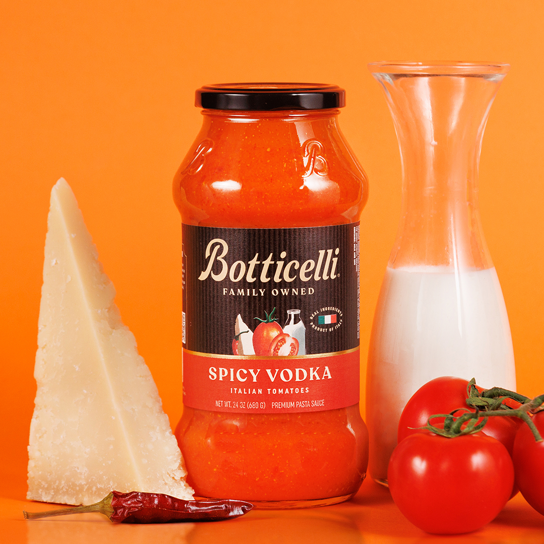 Botticelli Spicy Vodka bottle with Parmesan cheese, tomatoes, and a pepper on an orange background