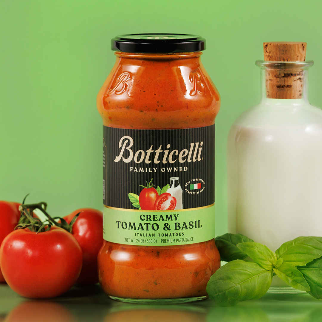 Jar of Botticelli creamy tomato and basil sauce with tomatoes and basil on a green background