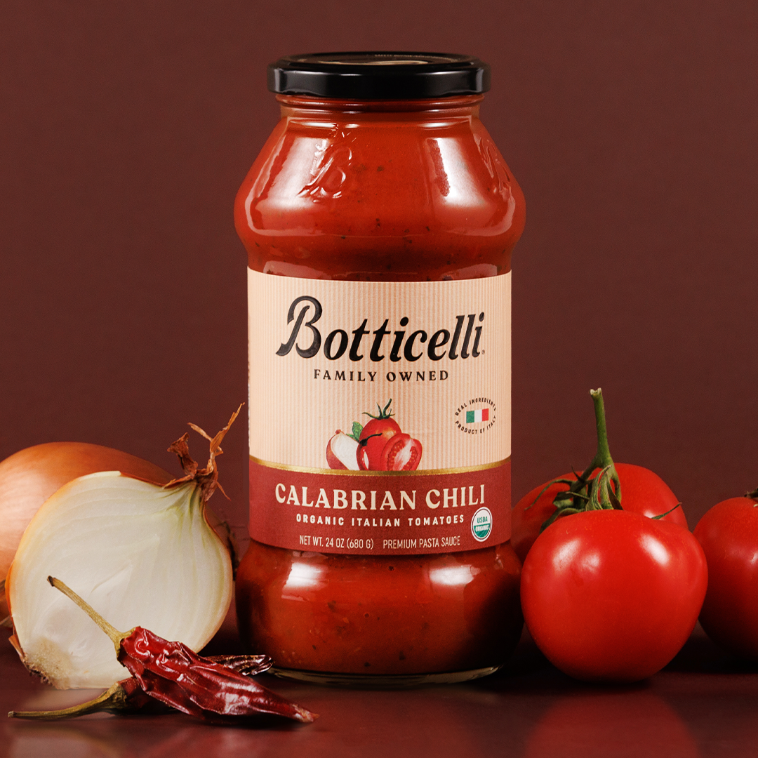 Botticelli Calabrian Chili pasta sauce jar with tomatoes and an onion on a red background