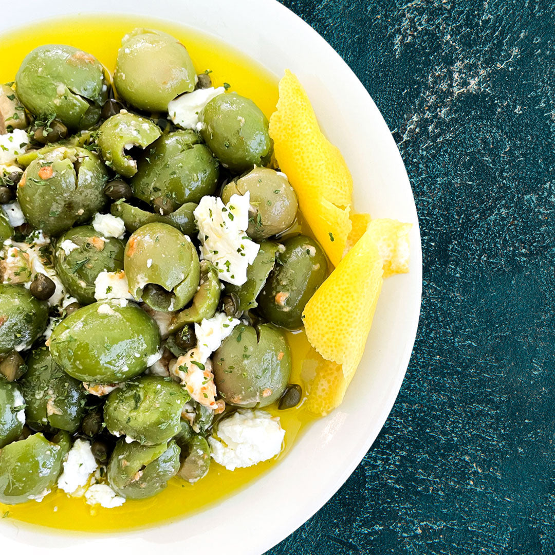 Green olive salad with lemon wedges on a white plate against a dark background