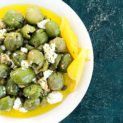 Green olive salad with lemon wedges on a white plate against a dark background