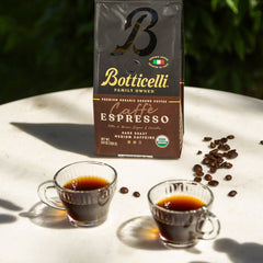 Botticelli Caffè Espresso coffee package with two cups of coffee and scattered beans on a light surface.
