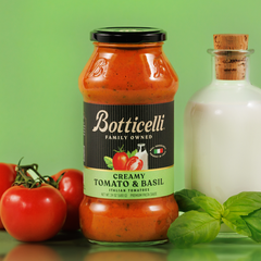 Jar of Botticelli creamy tomato and basil sauce with tomatoes and basil on a green background