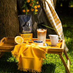 Botticelli coffee bag with a cup of coffee, lemon, and blueberries on a wooden tray outdoors.